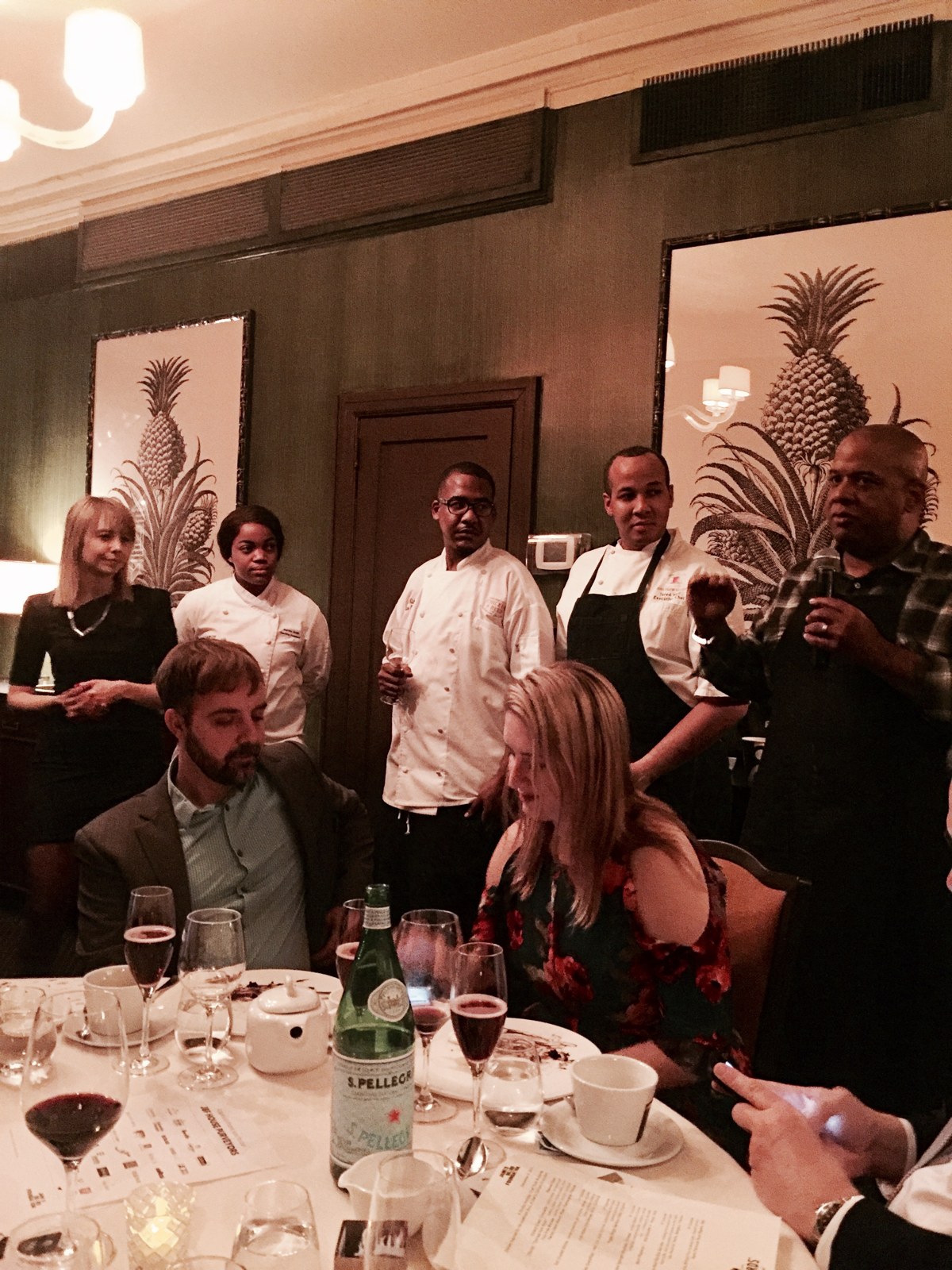 Chefs in white jackets gathered beside a speaker addressing guests at a James Beard House dinner.