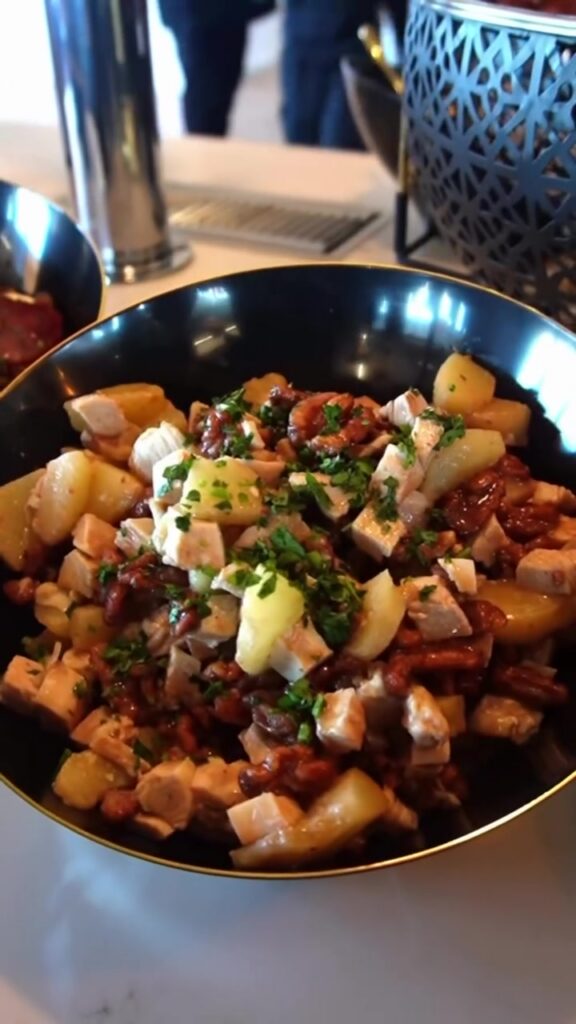A black serving bowl of diced potatoes topped with crumbled white cheese and chopped green herbs.